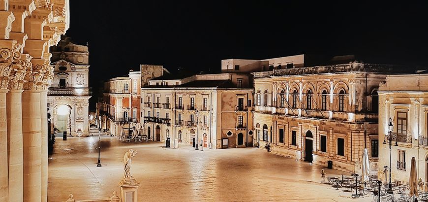Piazza Duomo on Ortigia lit at night, baroque facades along the square with the cathedral columns at the left