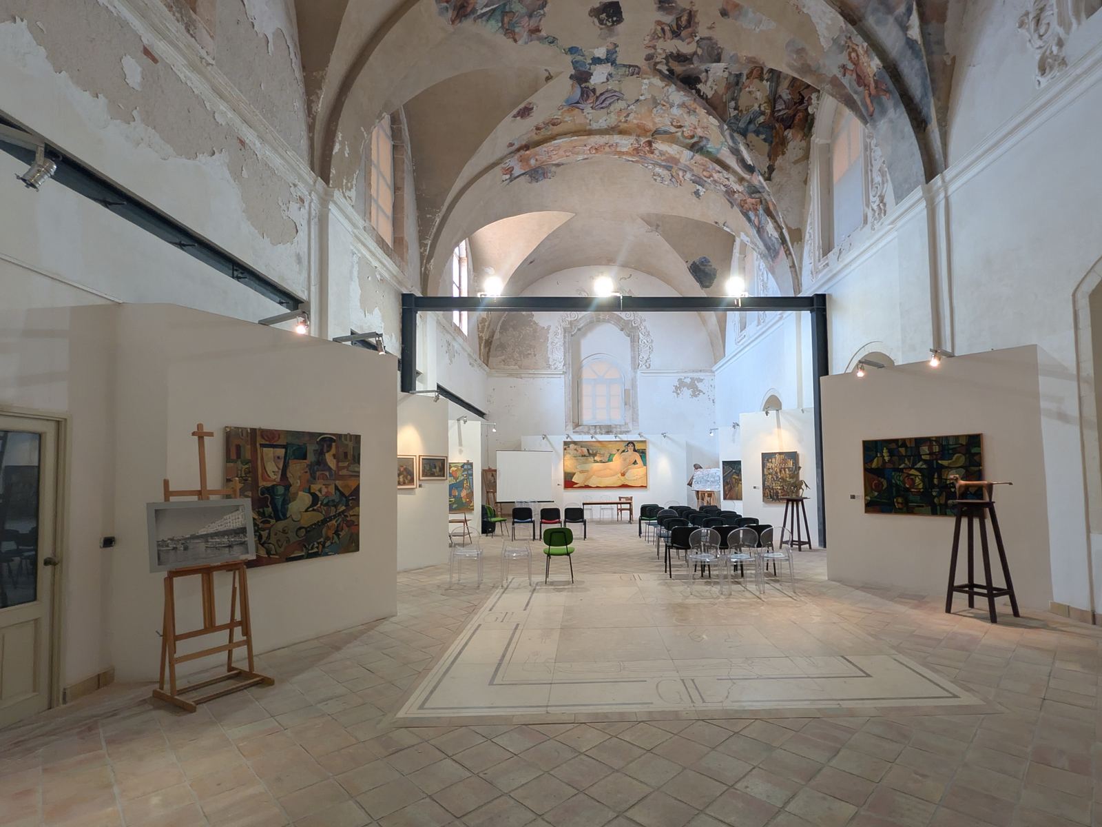 Spazio Novecento in the ex Convento del Ritiro: twentieth-century paintings under the frescoed vault, chairs set out in the nave