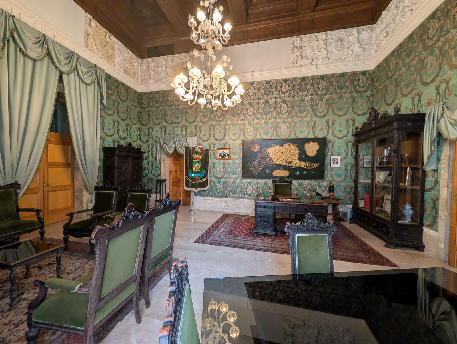The mayor's room at Palazzo Vermexio: green silk walls, a chandelier, the carved map of Ortigia behind the desk